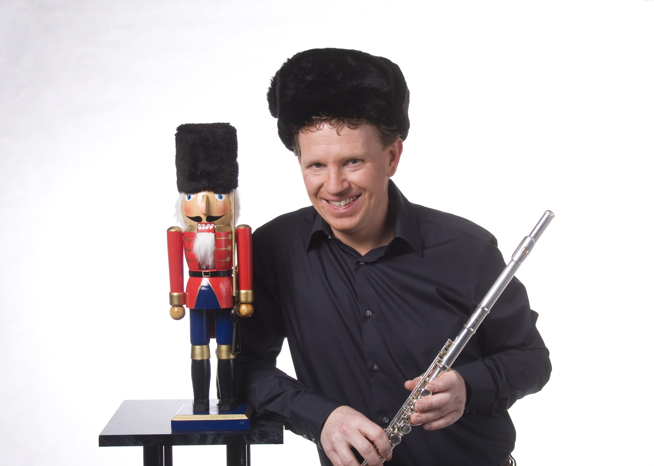 Man sieht einen Nussknacker aus Holz in den Farben rot und blau, der auf einem Podest steht. Neben ihm steht ein Musiker mit einer Querflöte in der Hand.