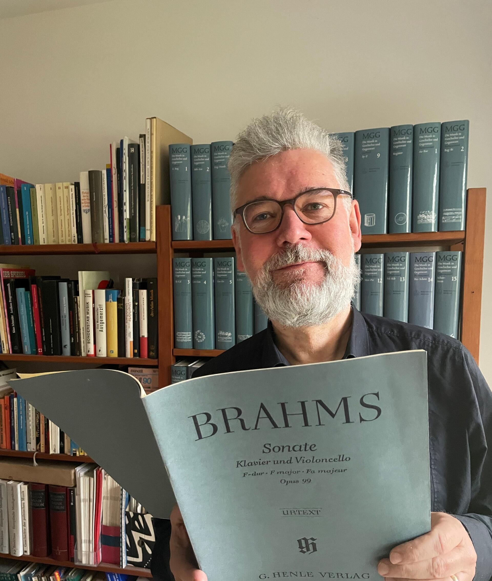 Tim Koeritz stands in front of a wall of books and holds a Brahms score in his hand.