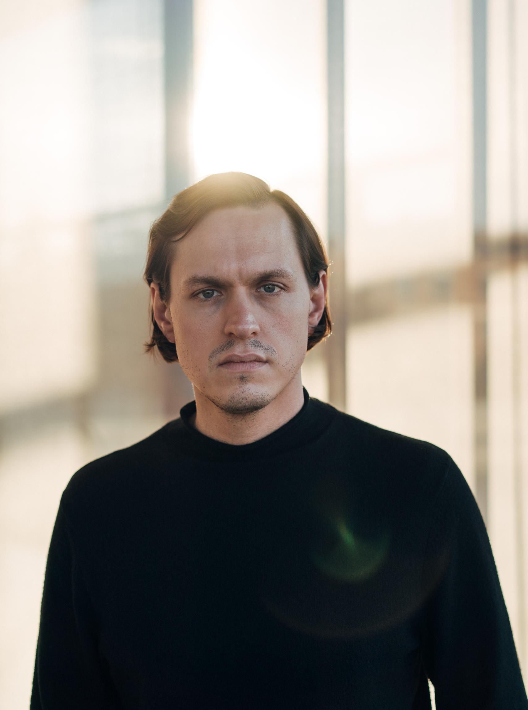 Pianist Lorenz Kellhuber wears a black sweater and looks into the camera with a serious expression.