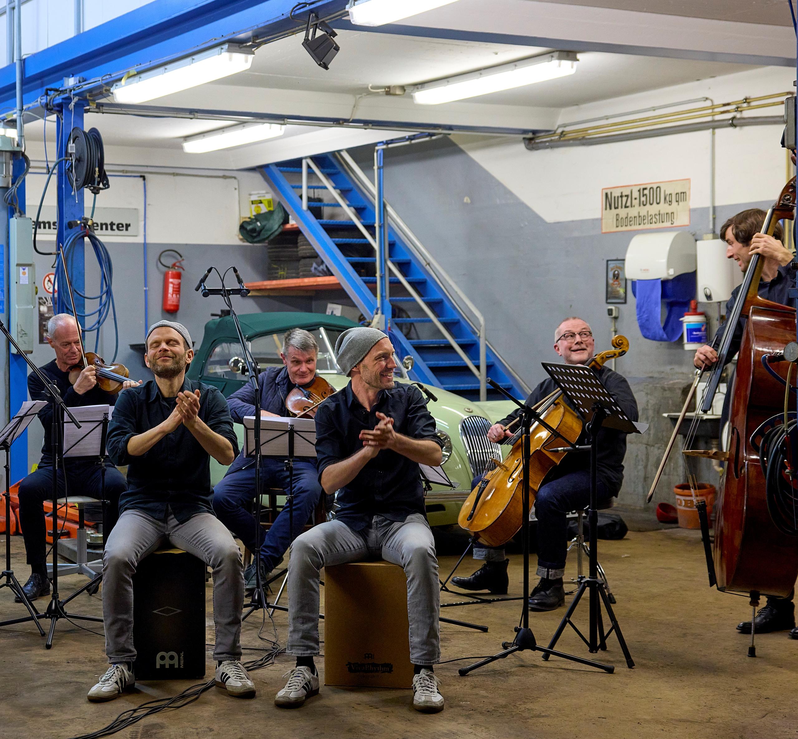 Classical musicians with two drummers in a car workshop