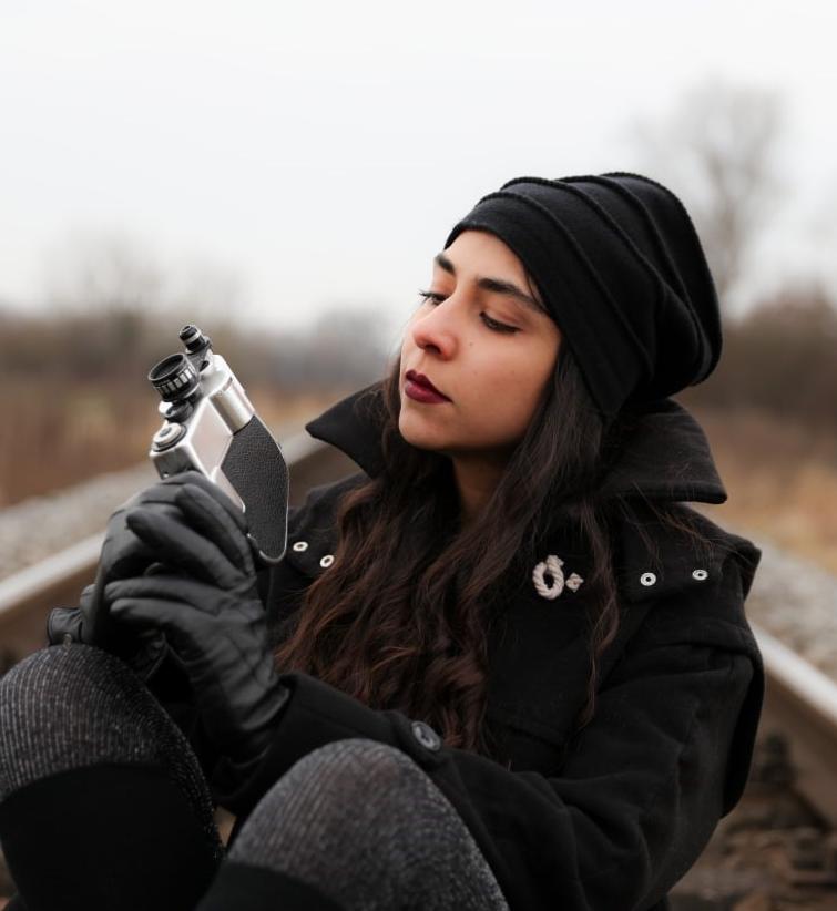 Mandana Behad hält eine Kamera in der Hand und sitzt in der Mitte eines Gleisbettes.