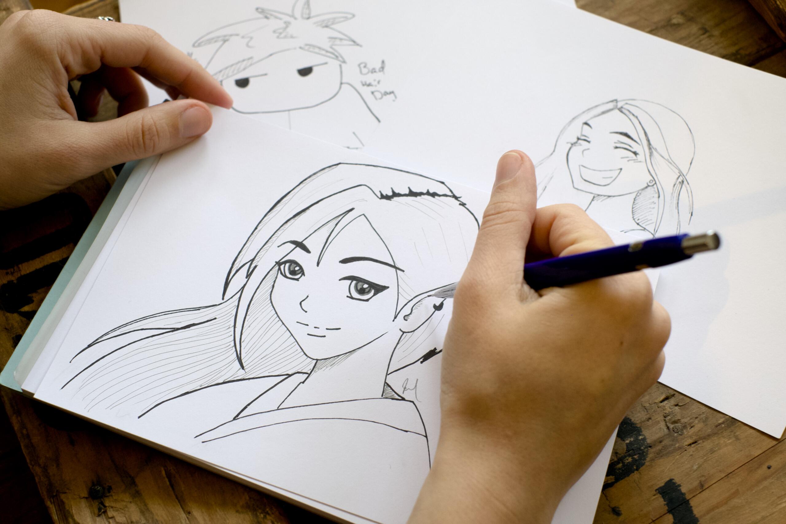 Man sieht ein Malpapier, auf dem eine Mangafigur abgebildet ist und eine Hand, die diese gerade zeichnet. 