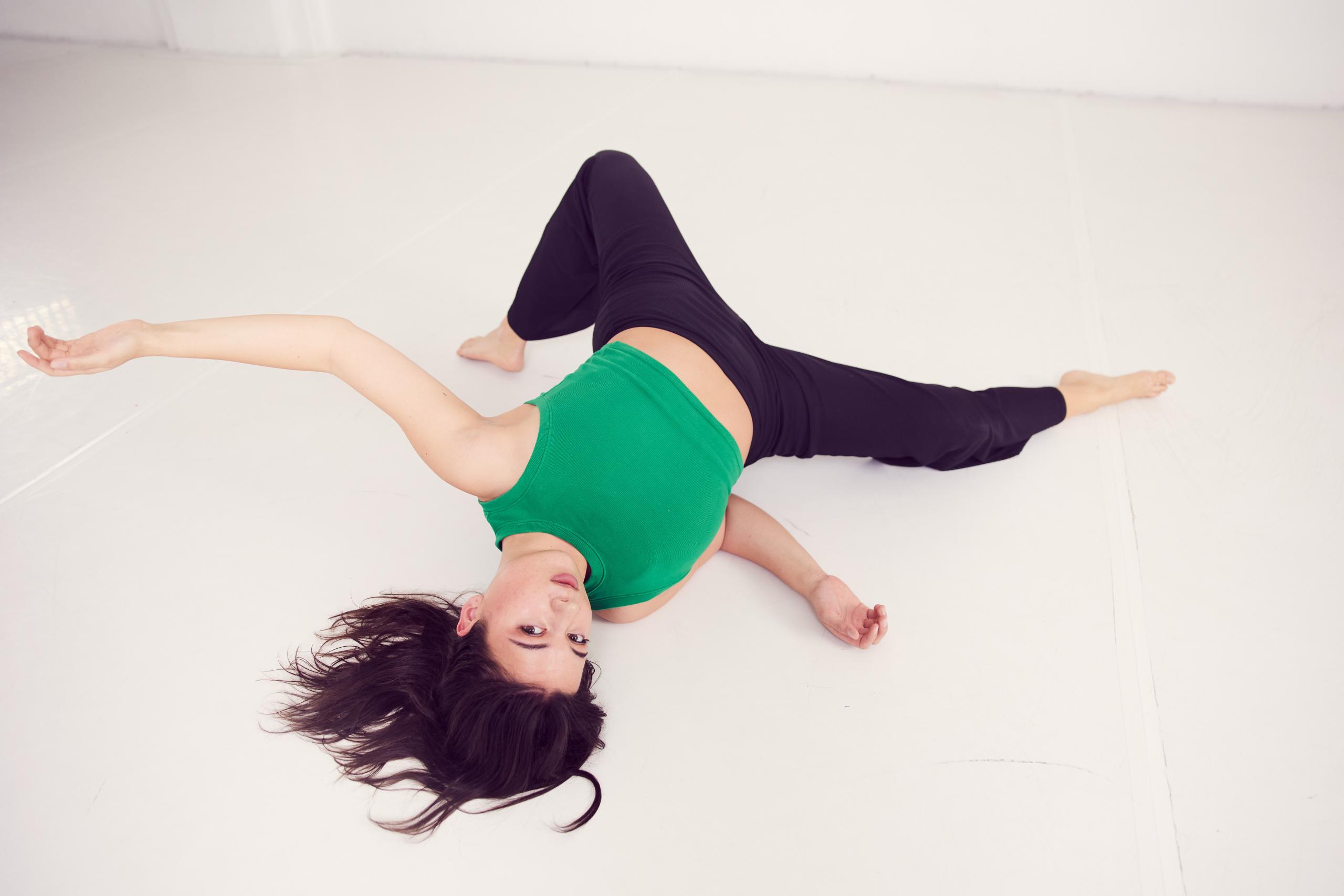 A young woman lies in a dancing pose on a white studio floor.