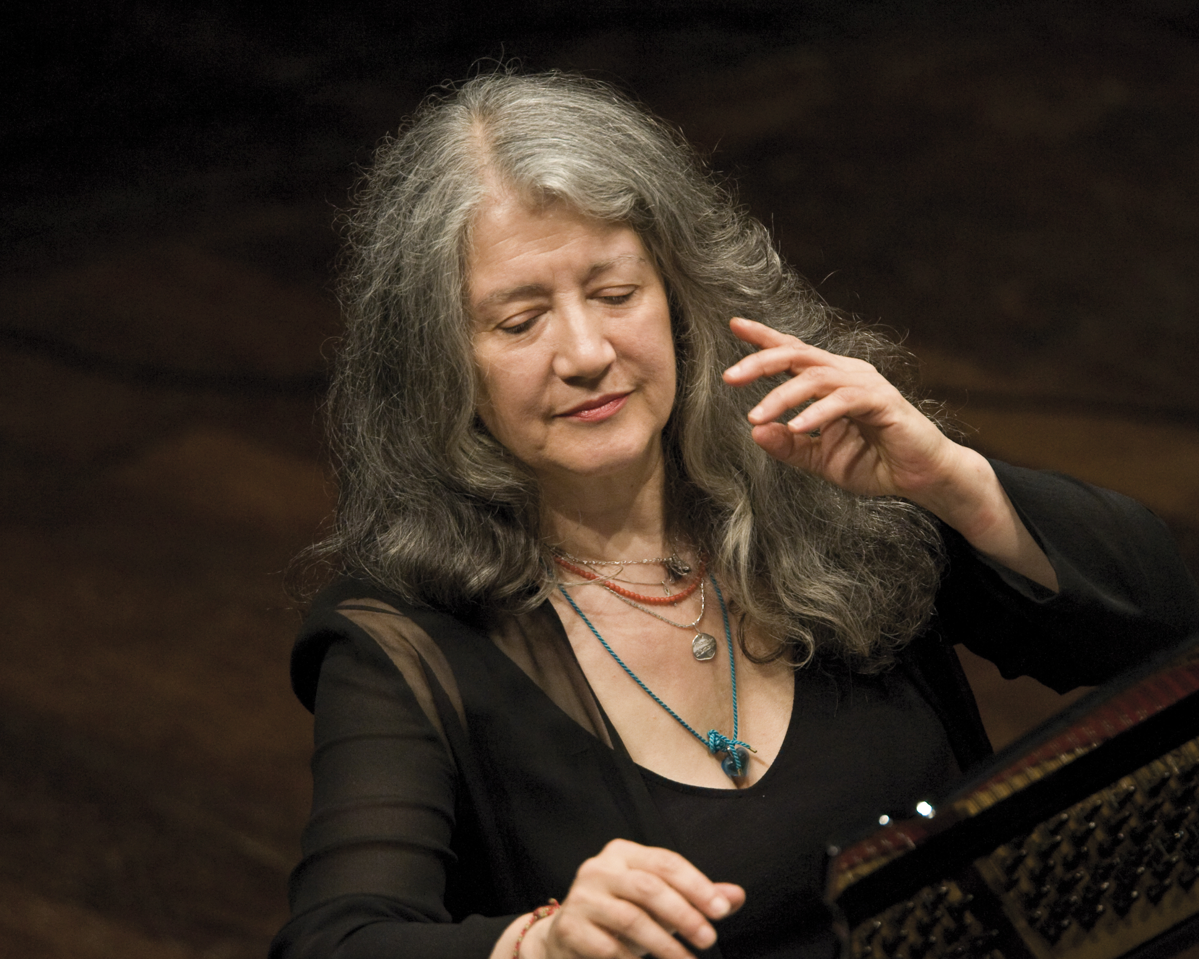Portrait shot of pianist Martha Argerich while playing the piano with both hands raised in one motion.