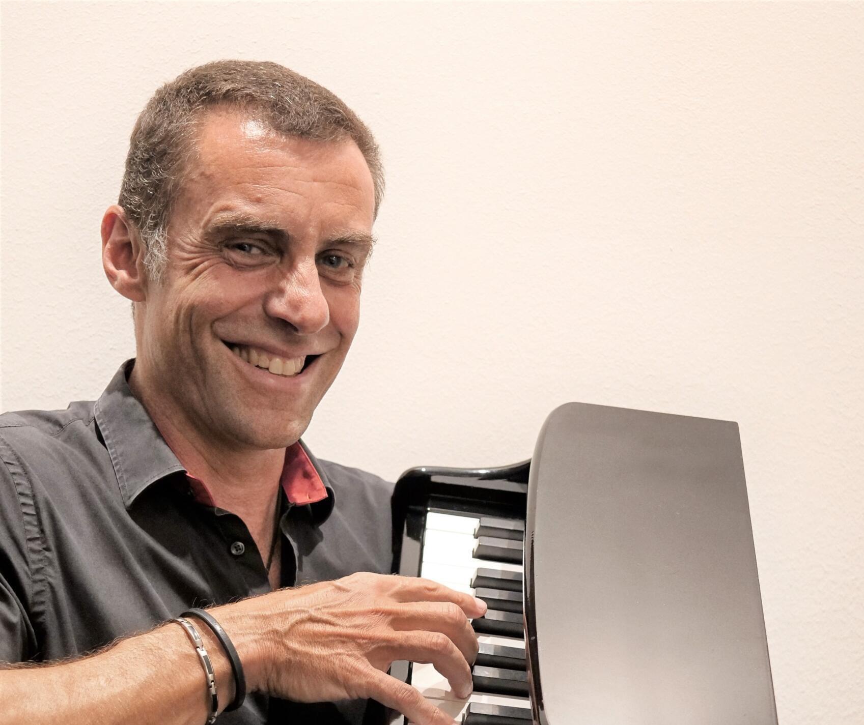 Picture of cabaret artist Martin Schmitt. He is wearing black clothing, smiling at the camera and holding a miniature piano.