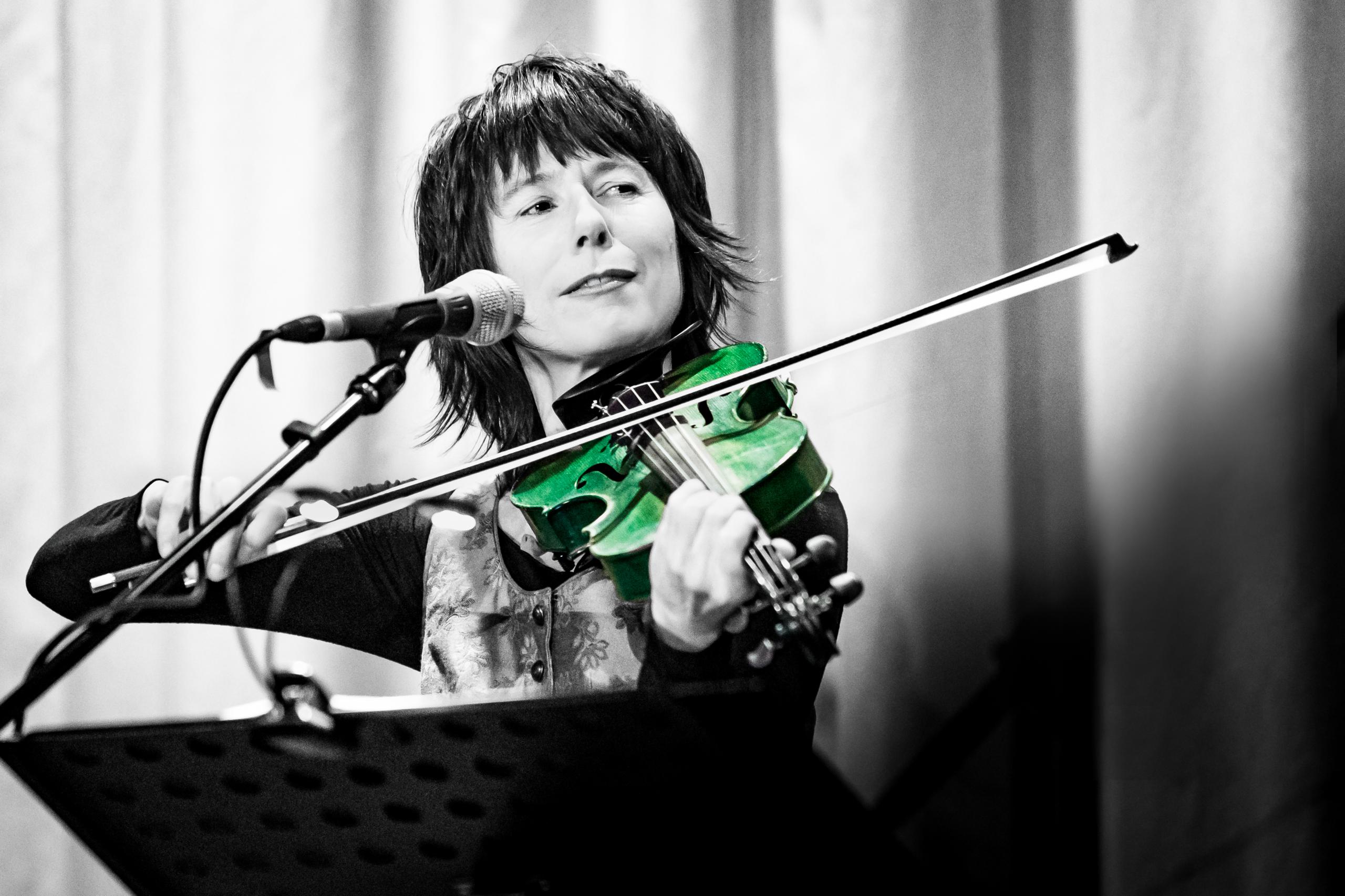 Die Musikerin Monika Drasch steht am Notenpult mit Mikro. Sie spielt Geige.