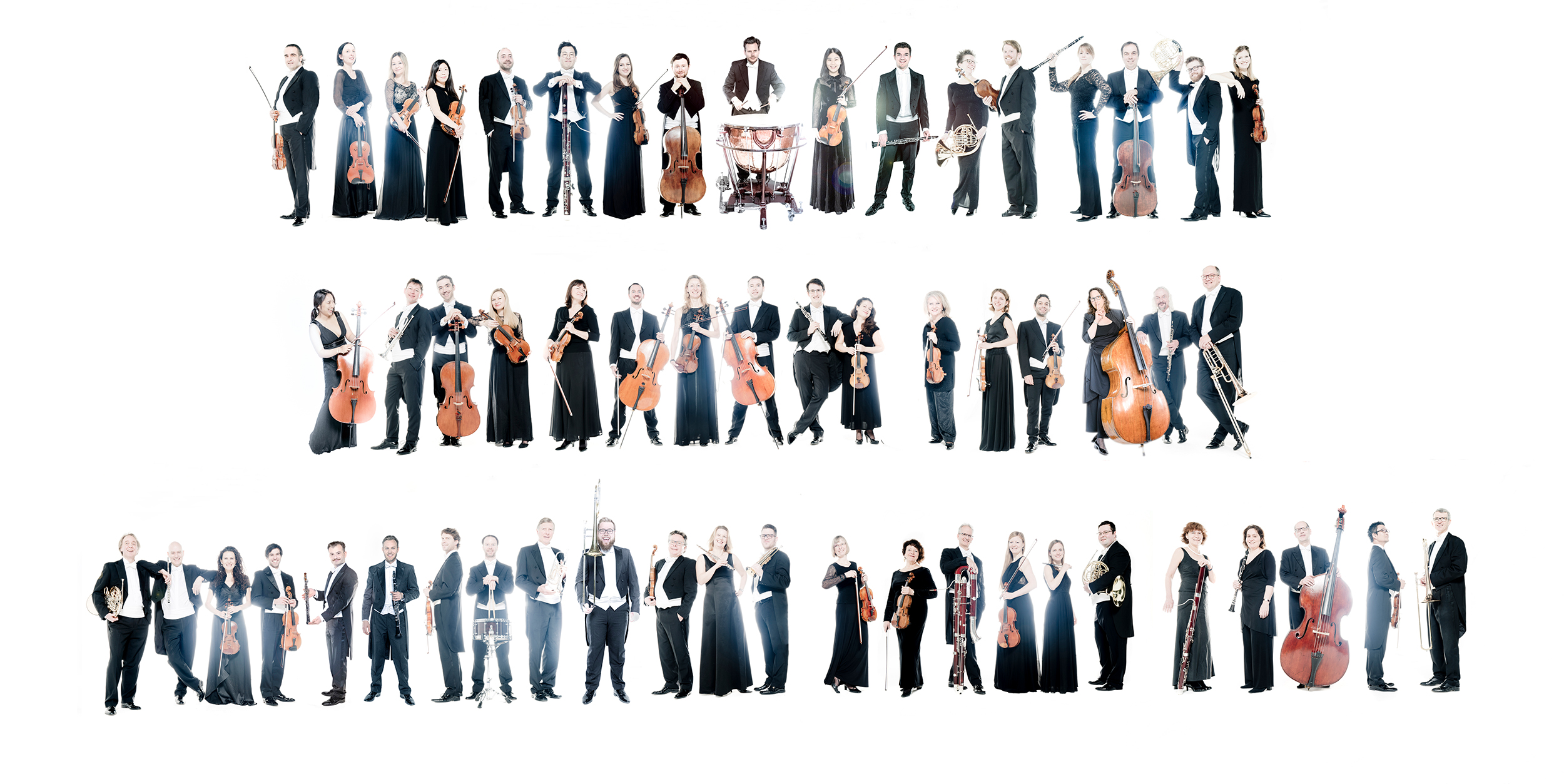 Die Musiker*innen mit ihren Instrumenten stehen in einer lockeren Reihe vor weißem Hintergrund.