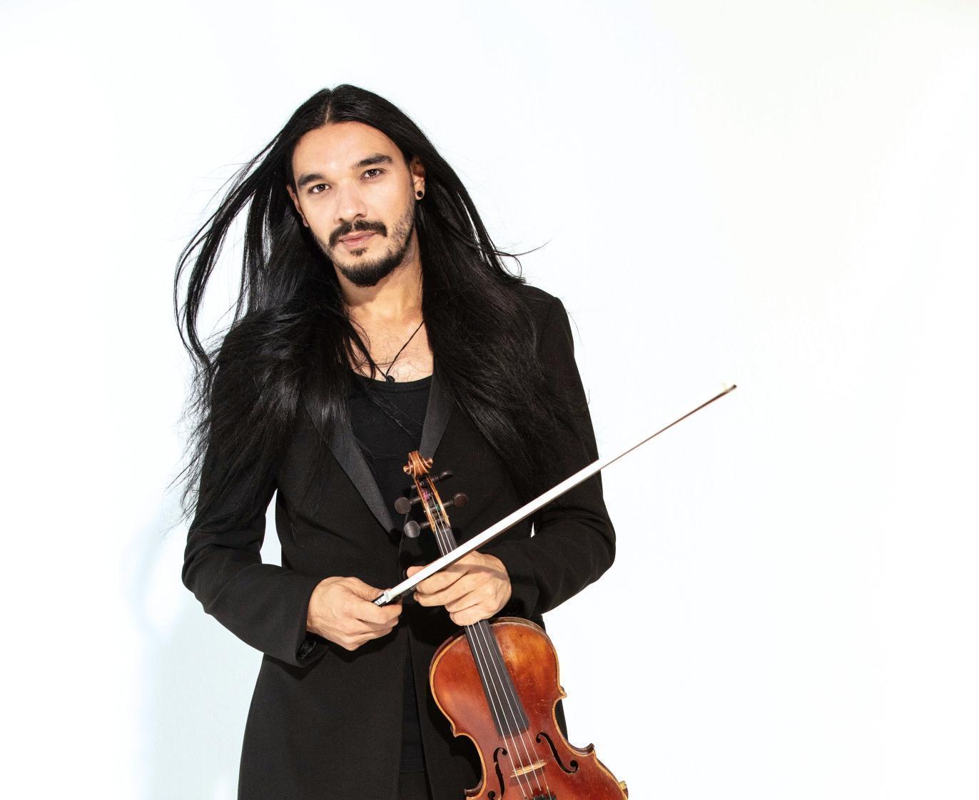 Violinist Nemanja Radulovic faces the camera head on, holding his instrument and bow in his hand