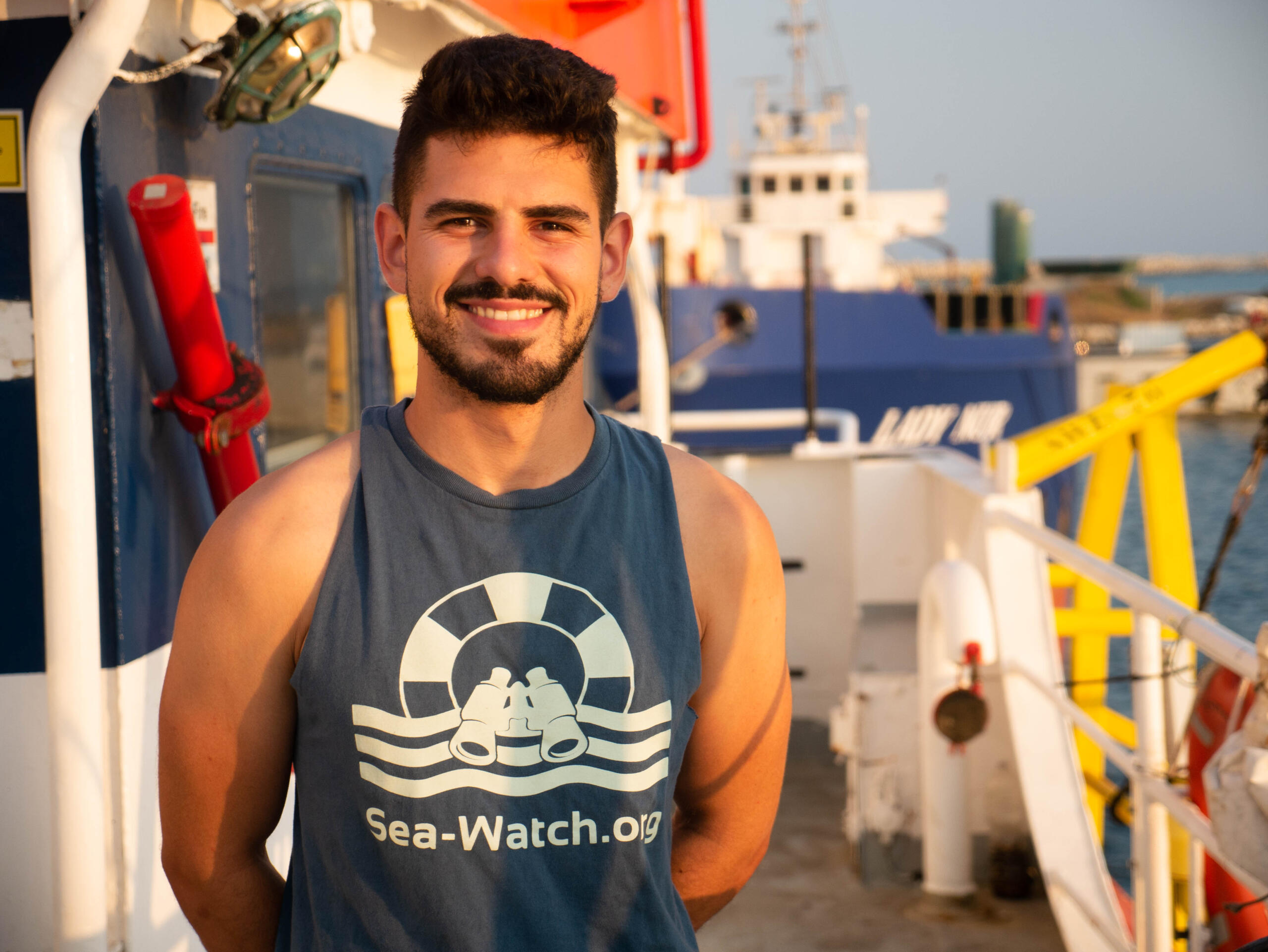 Adrian Pourviseh steht auf einem Schiff und trägt ein See-Watch-Shirt.