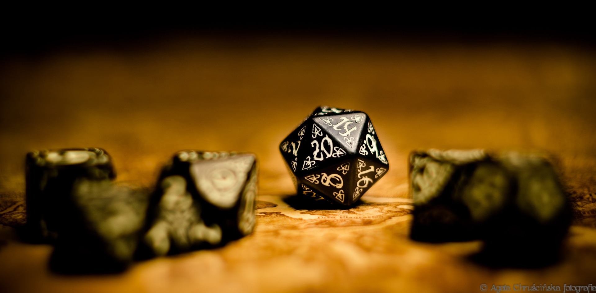 Schwarze Würfel mit weißen Runen liegen auf einem goldenen Spielfeld.