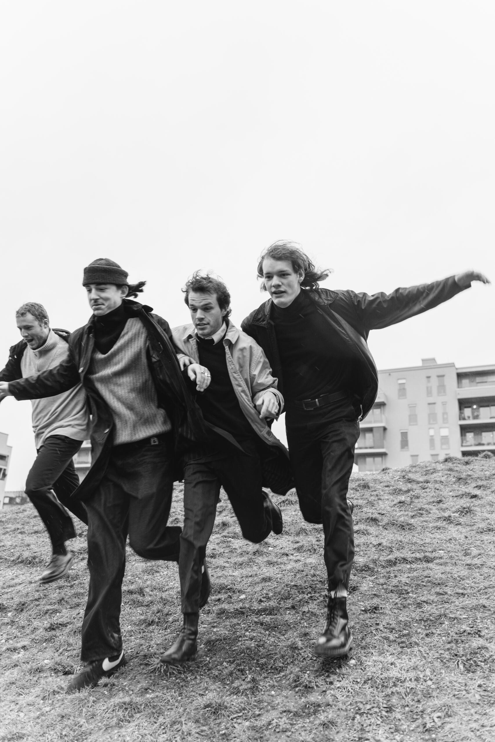 Four young men run down a grassy hill.