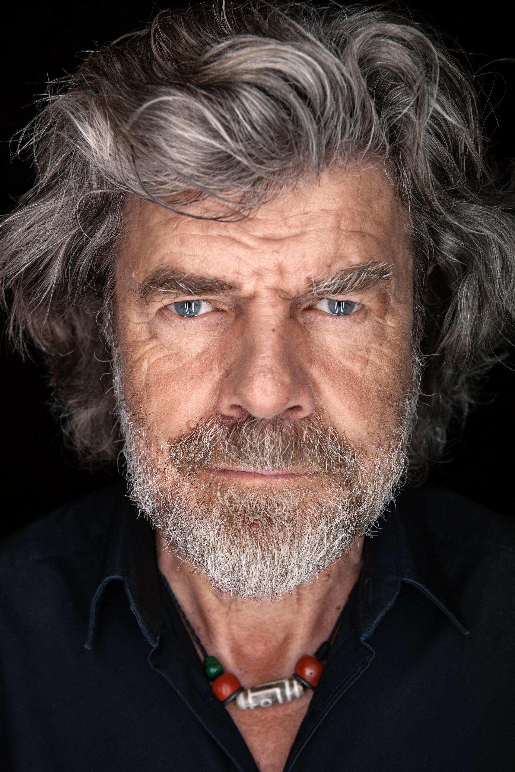 Close-up of mountaineer Reinhold Messmer looking directly into the camera with wild gray hair and gray-blue eyes.