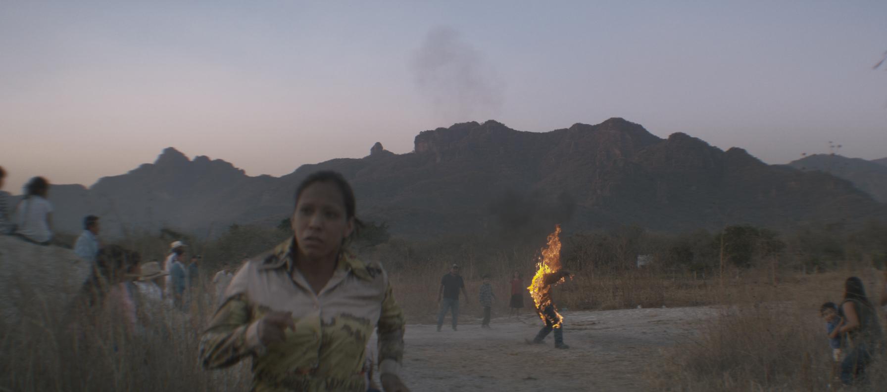 A woman runs away from a scene where several other people are looking at a person on fire.