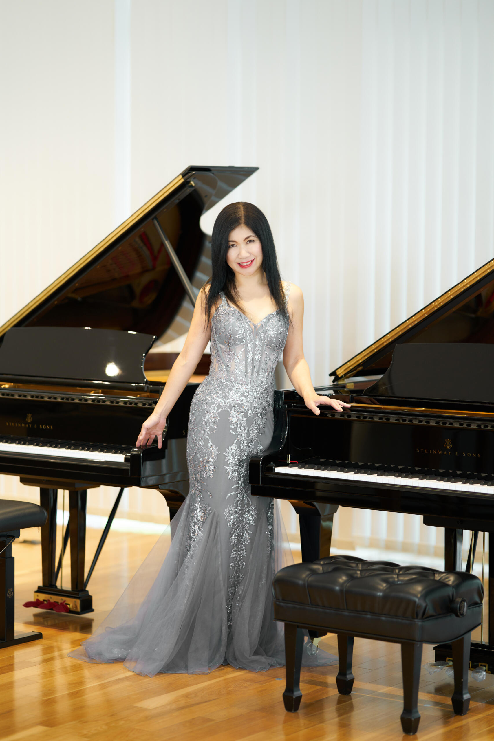 A lady in a glittering evening dress leans against a grand piano.