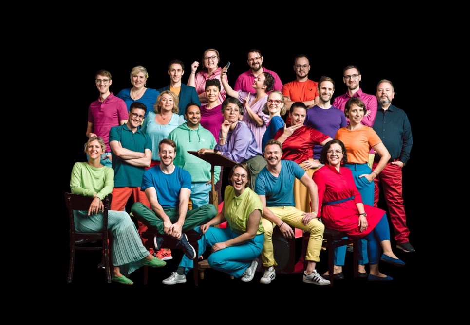 Picture of the a cappella choir SoulFood Delight. All members of the choir are wearing brightly coloured clothing. The background is black.