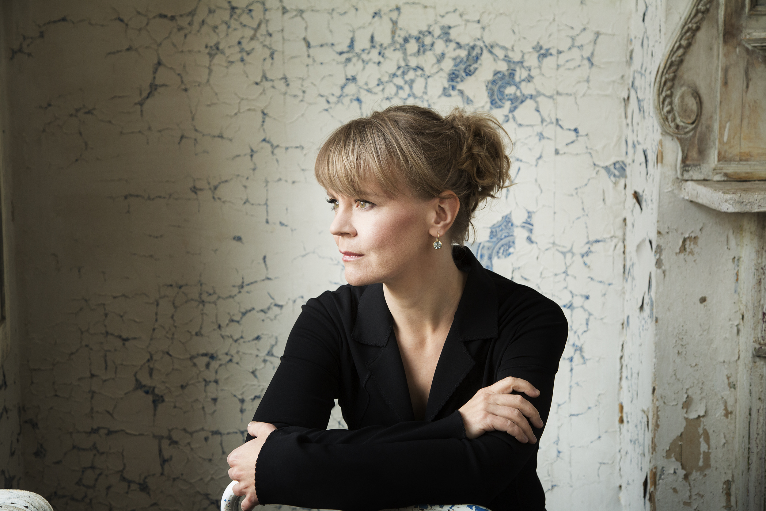  Conductor Susanna Mälkki leans on the back of a chair with her arms crossed and looks to the side