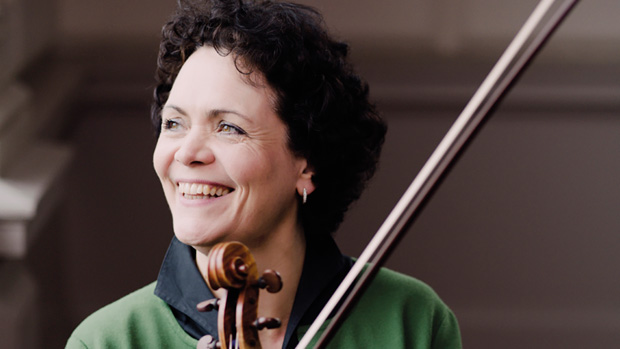 Tabea Zimmermann hält eine Violine in der Hand und lacht in die Kamera. 