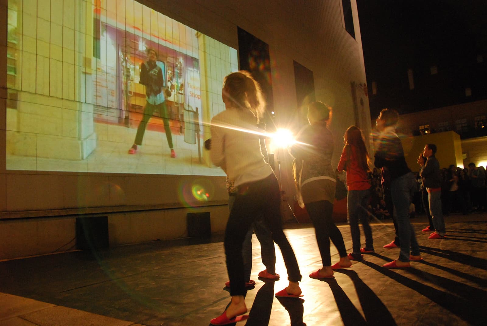 Menschen tanzen in einer Reihe, ihr Blick geht an eine Wand, auf der ein Video projiziert wird.