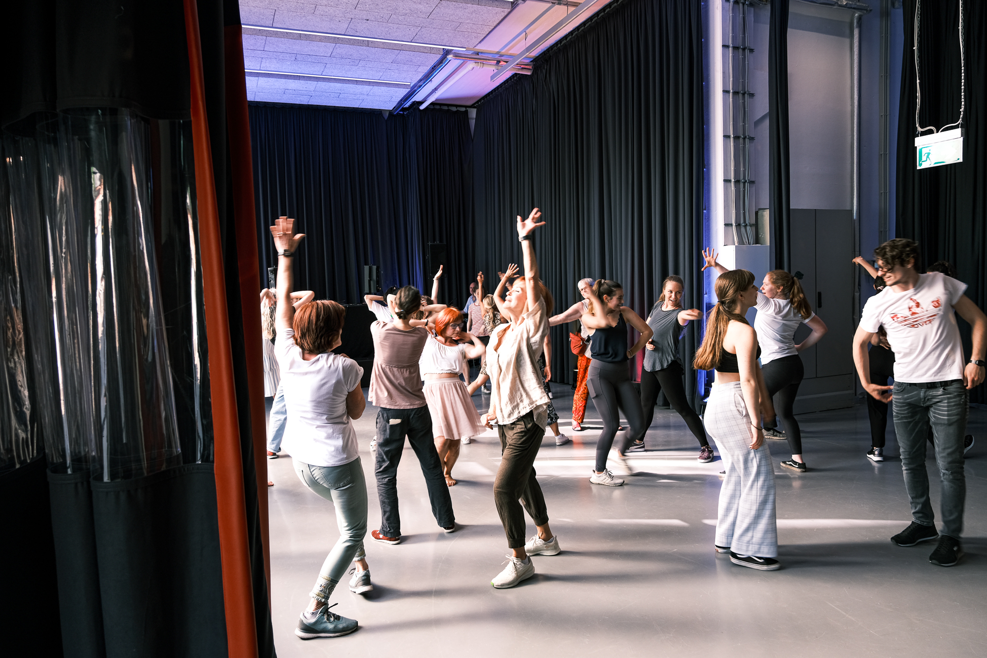 Large room with dark curtains from ceiling to floor, in the center of the picture people making dance movements
