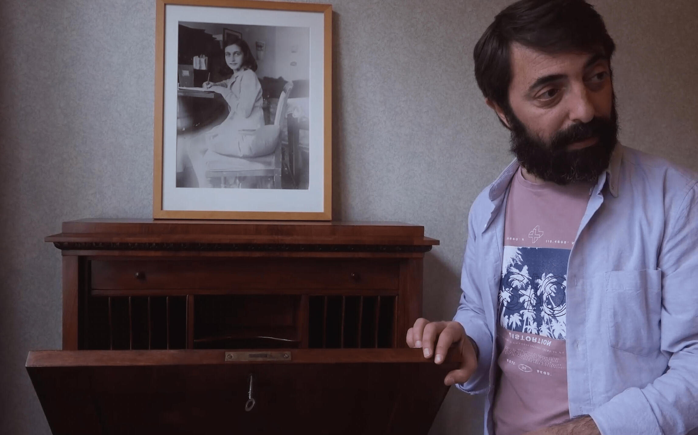 A man is standing next to an old chest of drawers with a picture of Anne Frank on it.