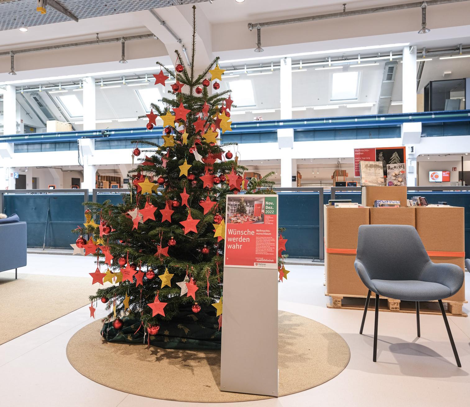 Weihnachtlicher Wunschbaum mit roten und gelben Sternen in der Halle E im Gasteig HP8. Auf den Sternen sind Wünsche bedürftiger Münchner*innen notiert.