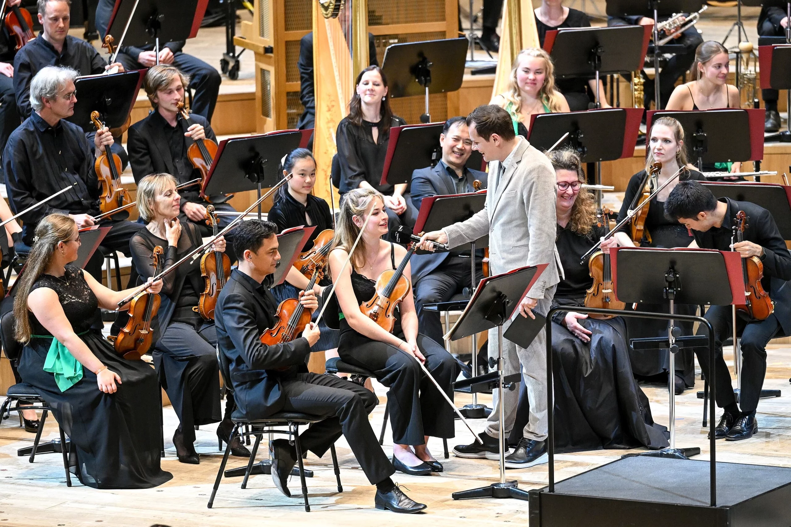 Young people from the Odeon Youth Symphony Orchestra sit on the stage of the Isarphilharmonie and are interviewed by presenter Malte Arkona.