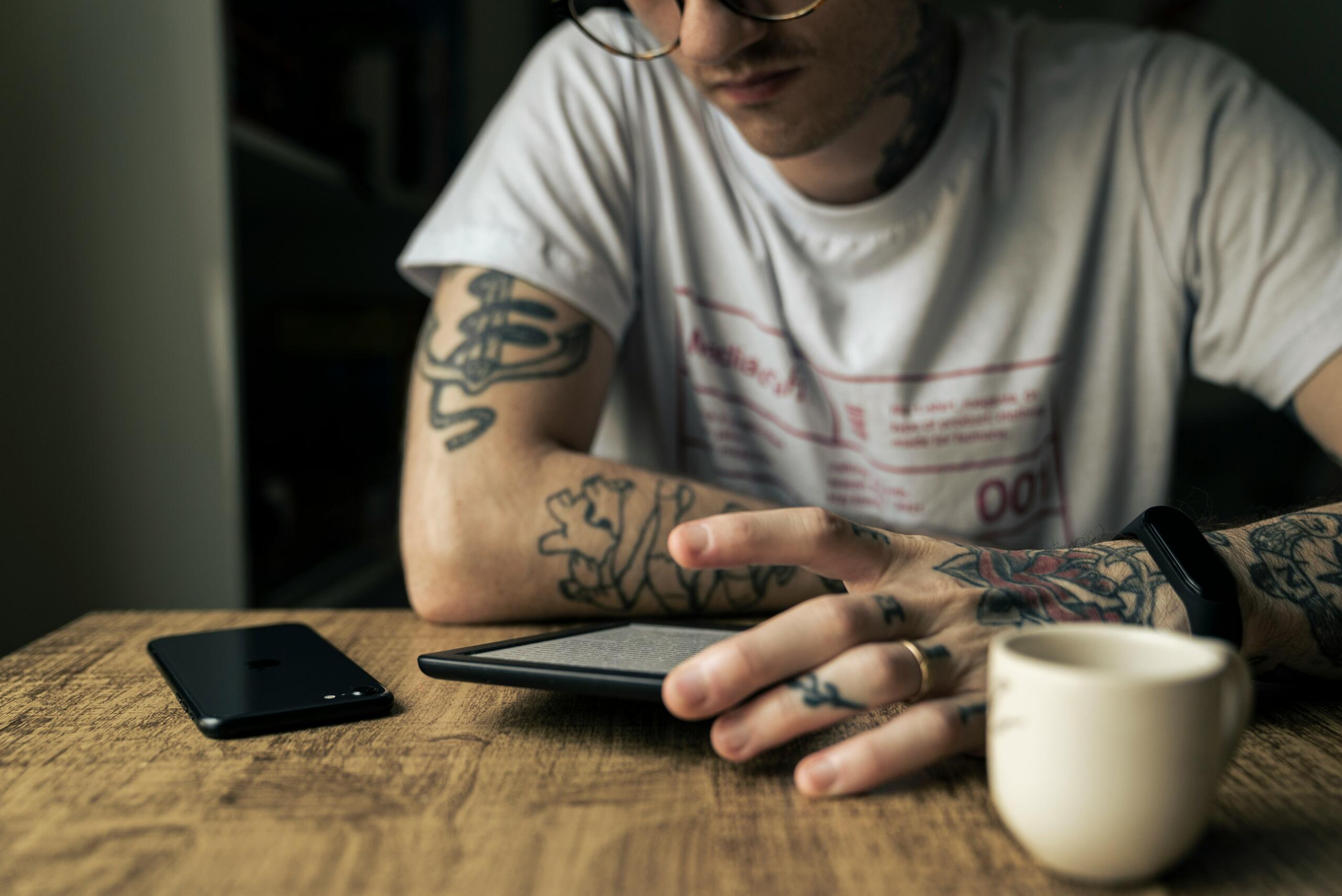 Junger Mann mit tätowierten Armen schaut auf einen E-Reader.
