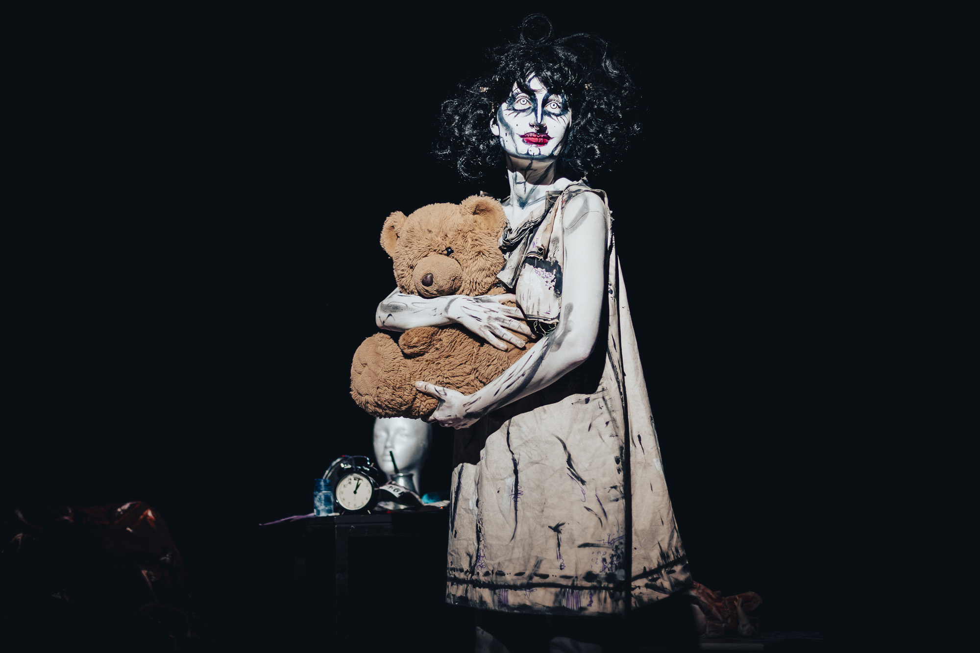 A person with comic-like make-up is holding a teddy bear.