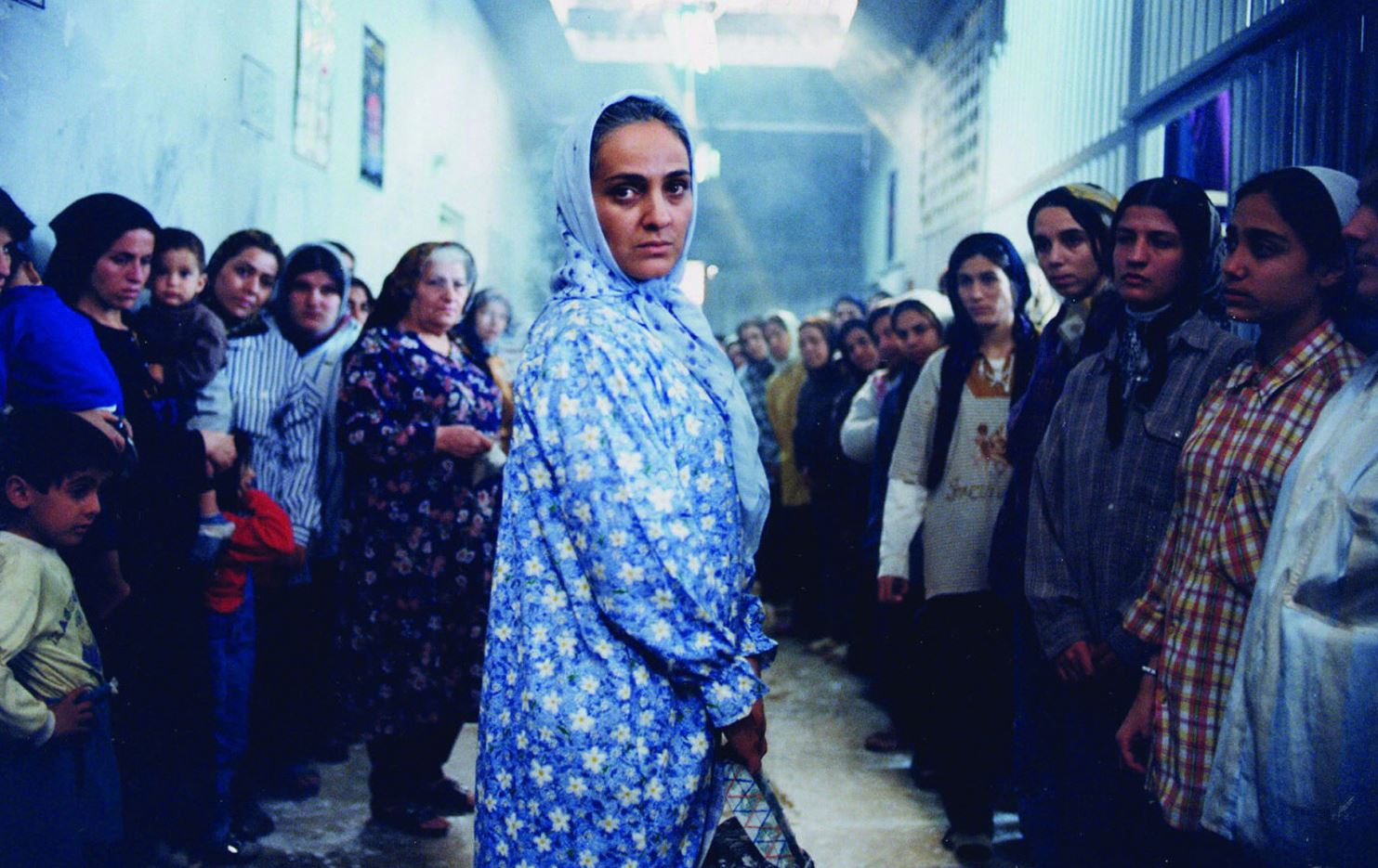 Eine iranische Frau mit Kopftuch steht in der Mitte des Bildes, andere Frauen bilden eine Spalier.