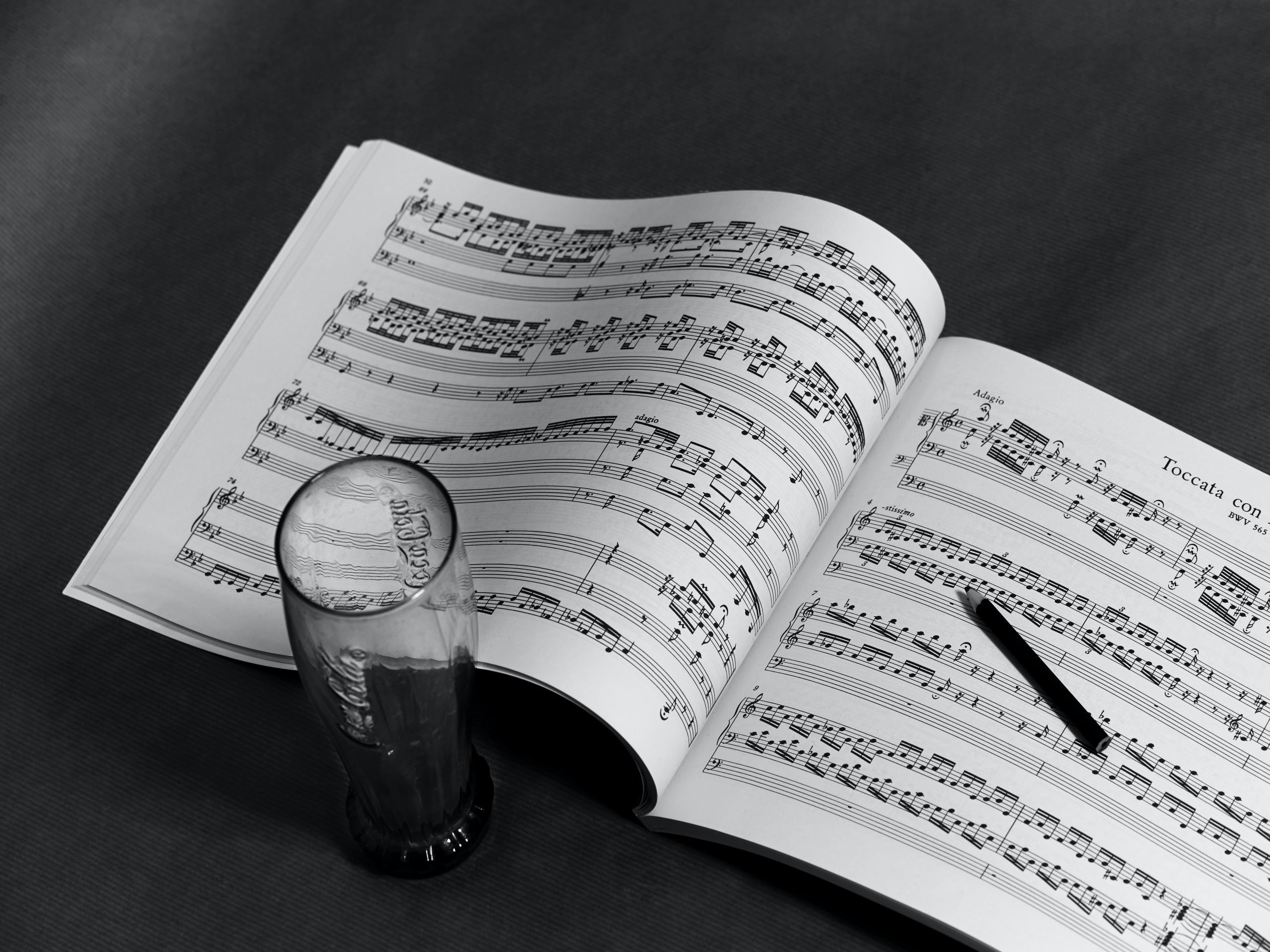 Aufgeschlagenes Heft mit Musiknoten, ein Wasserglas und ein Bleistift